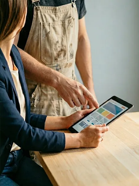 Webdesignerin zeigt einem Handwerker in Arbeitskleidung Website-Entwürfe auf einem Tablet